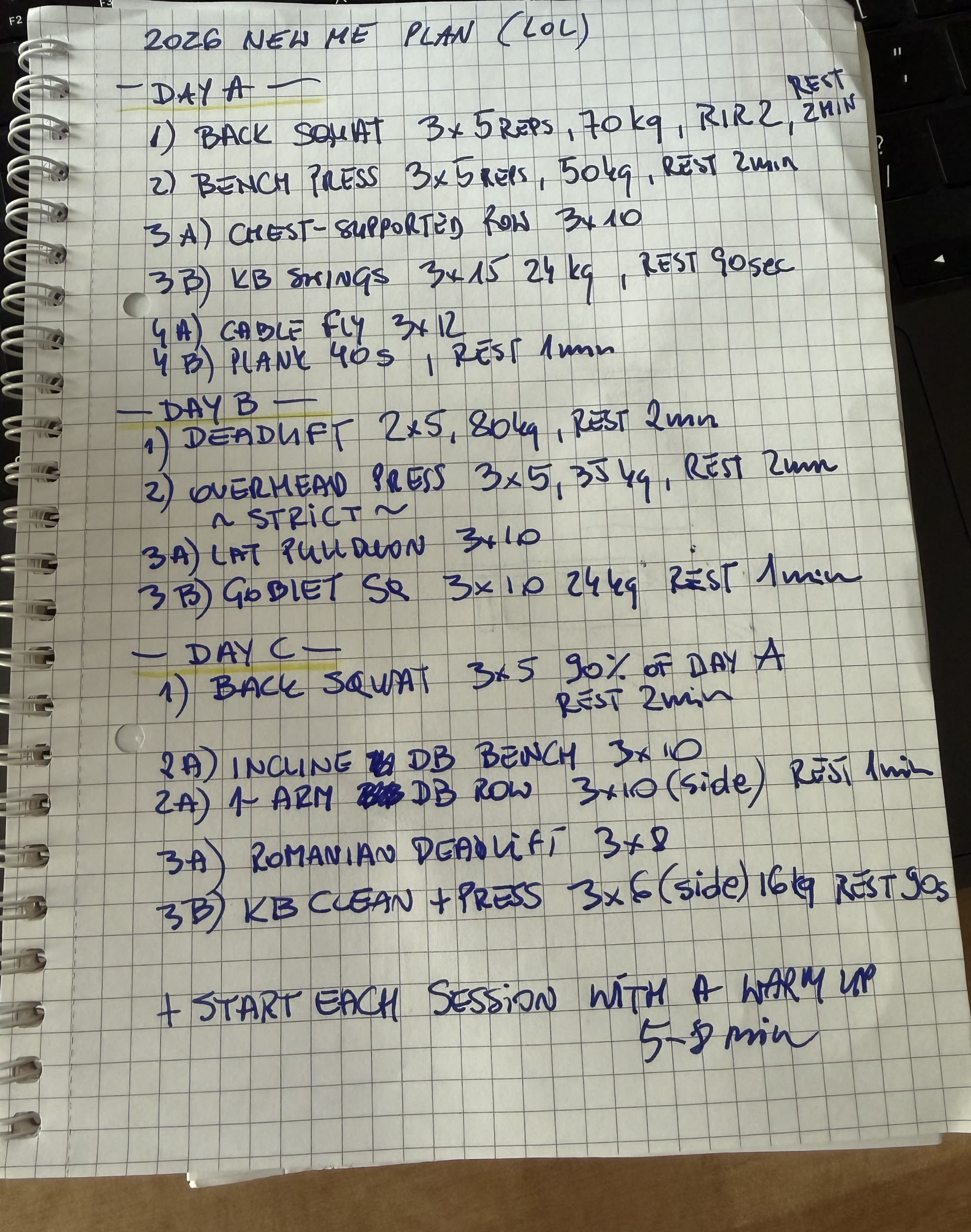 A handwritten 3-day workout plan on grid paper in a spiral notebook, titled "2026 New Me Plan", photographed at an angle on a desk with a keyboard in frame.